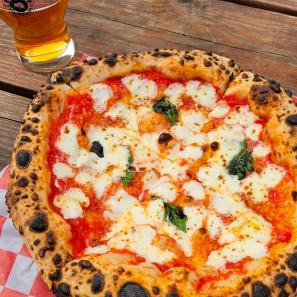 BareBakedPizza's Margherita pizza with a charred crust, fresh mozzarella, tomato sauce, and basil, next to a beer.