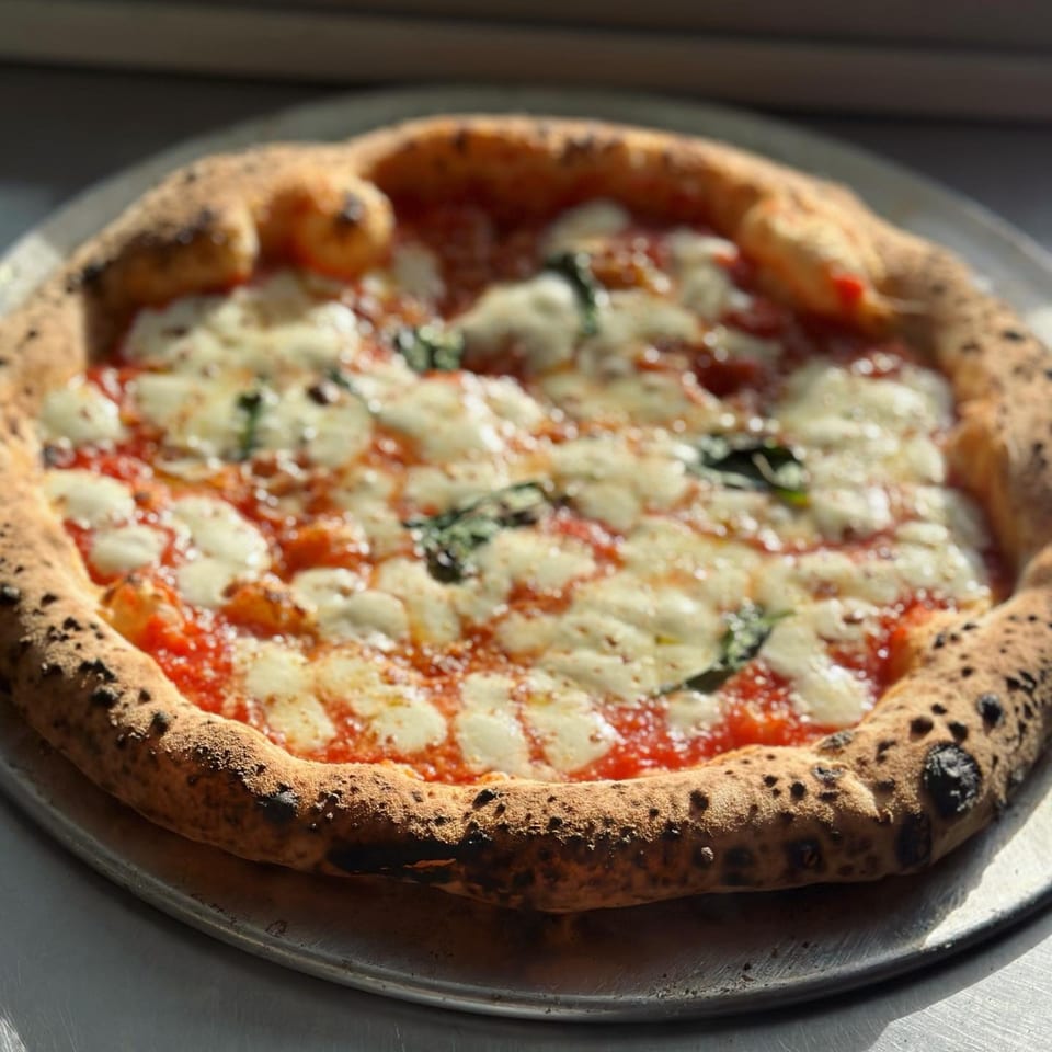 BareBakedPizza's Margherita pizza with melted mozzarella, red sauce, and fresh basil on a metal tray.