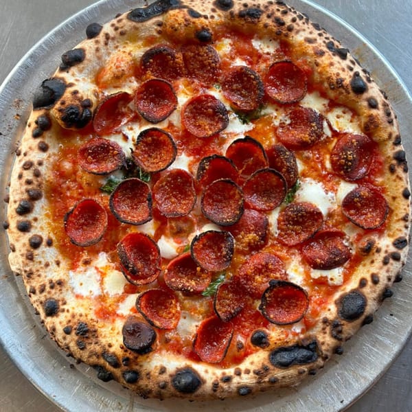 BareBakedPizza pepperoni pizza with a charred crust, melted cheese, and tomato sauce on a metal tray.