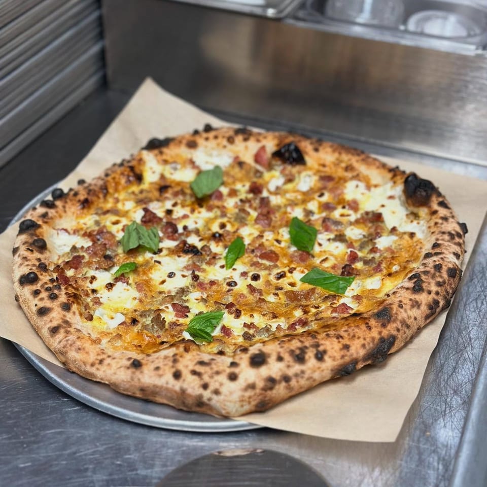 BareBakedPizza's pizza with white sauce, bacon, sausage, and basil on a metal tray.