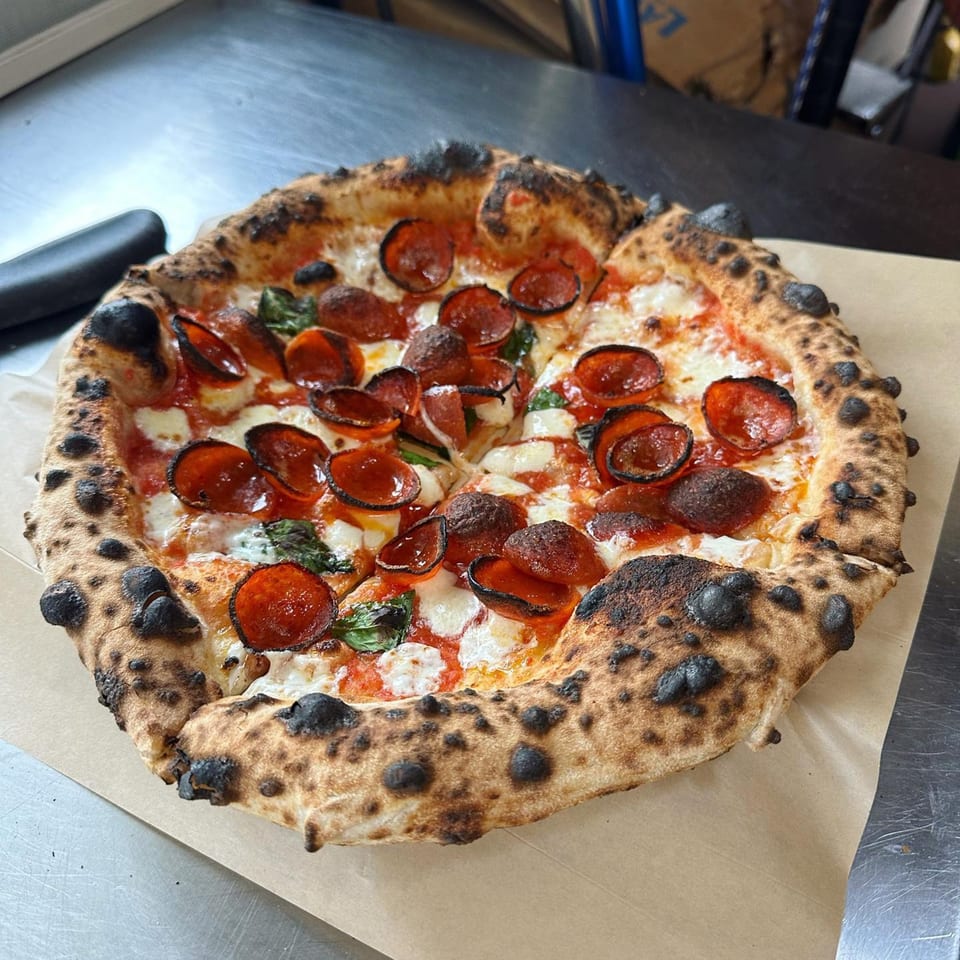 A BareBakedPizza pepperoni pizza with a charred crust, fresh basil, and melted mozzarella cheese.