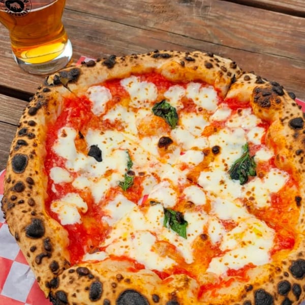 BareBakedPizza's Margherita pizza with fresh mozzarella, basil, and a perfectly charred crust next to a beer.