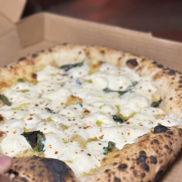 BareBakedPizza's white pizza with melted cheese and green herbs in a cardboard box.
