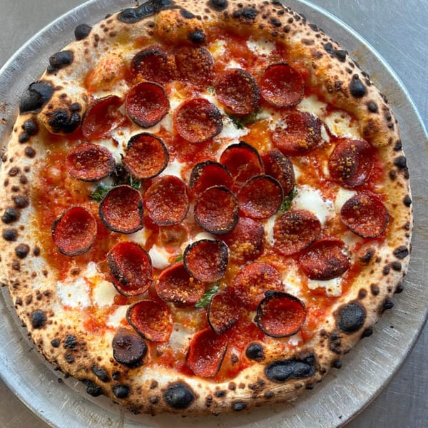 A BareBakedPizza pepperoni pizza with a charred crust, melted cheese, and tomato sauce on a metal tray.