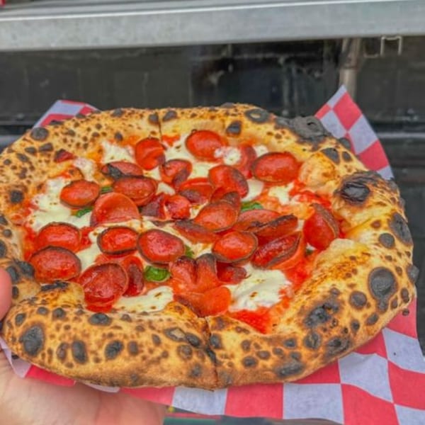BareBakedPizza's pepperoni pizza with a perfectly charred crust, fresh mozzarella, and basil on checkered paper.